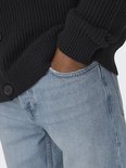 Close-up van een man met zijn hand in de zak van een lichtblauwe jeans, met knopen zichtbaar.