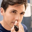 Een man met donker haar gebruikt een zwarte Philips neustrimmer om zijn neusharen te trimmen.
