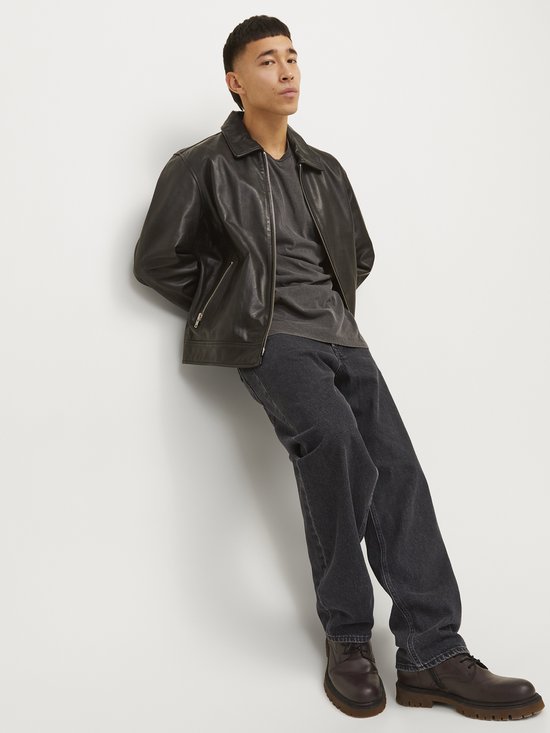 Model draagt losse, zwarte jeans met leren jack.