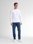Model draagt een wit shirt en blauwe tapered fit jeans met witte sneakers.