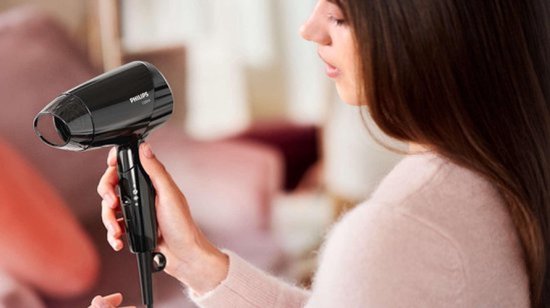 Vrouw met lang bruin haar houdt een zwarte Philips föhn vast.