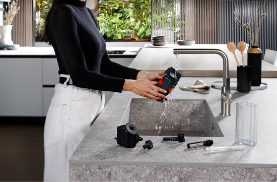 Vrouw spoelt de zetgroep van een DeLonghi volautomaat onder de kraan.