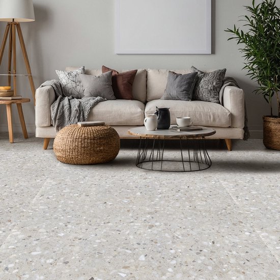 Woonkamer met lichte bank, kussens, salontafel en planten, op een terrazzo vloer.