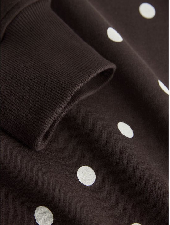 Close-up van de mouw van een donkerbruine sweater met witte polkadotprint en geribde manchet.