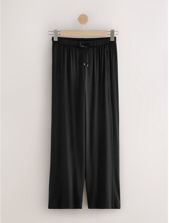 Zwarte wijde joggingbroek aan een kledinghanger.