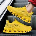 Gele sneaker met oranje vlammenprint op de zijkant en opengewerkte zool, gedragen op een roltrap.