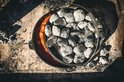 Gietijzeren pan met oranje stoofpot, bedekt met kolen, gezien van bovenaf.