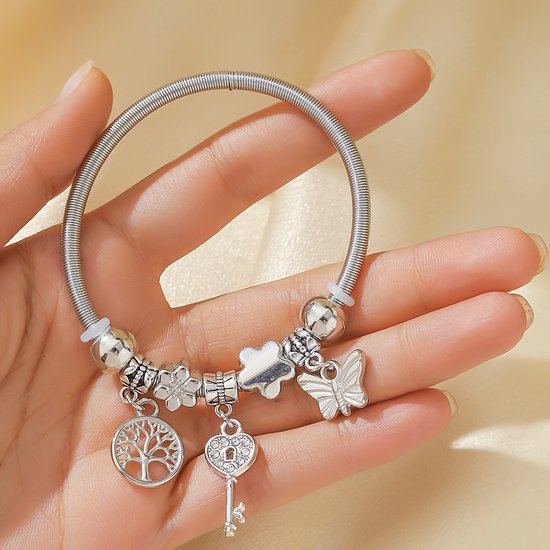 Zilverkleurige armband met spiraaldesign en bedels van een boom, hartsleutel, bloem en vlinder.