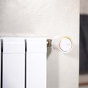 Netatmo slimme thermostaatknop, wit met oranje accent, op een moderne witte radiator.