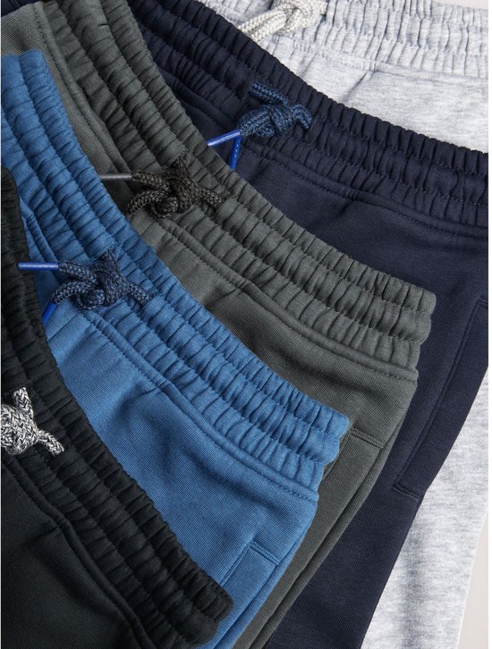 Detailopname van de taillebanden van vijf joggingbroeken in diverse kleuren met trekkoorden.