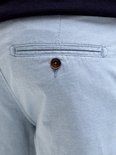 Detail van een achterzak met knoopsluiting op een lichtblauwe pantalon met ruitpatroon.