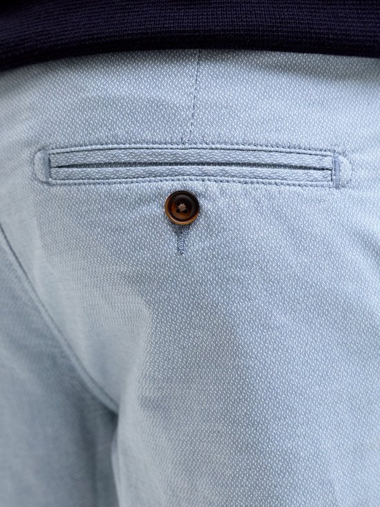 Detail van een achterzak met knoopsluiting op een lichtblauwe pantalon met ruitpatroon.