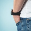 Zwarte imoshion smartwatchband om pols van persoon met witte t-shirt en spijkerbroek.