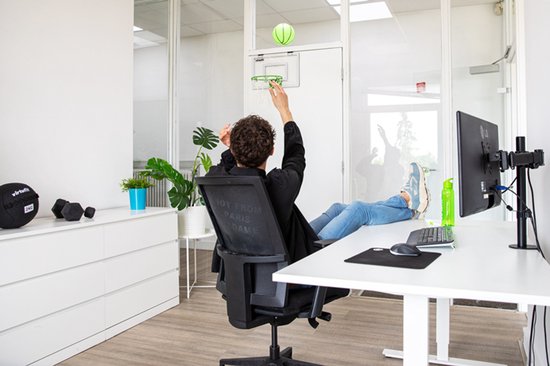 Man in kantoor gooit groene basketbal naar bord.