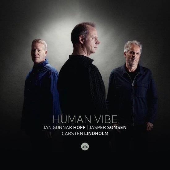 Drie mannen staan op een donkere achtergrond. De titel is "HUMAN VIBE JAN GUNNAR HOFF | JASPER SOMSEN CARSTEN LINDHOLM".