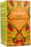 Pukka trois gingembres biologische thee verpakking met oranje achtergrond, gember bloemen en bladeren.