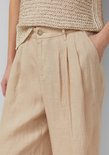 Detailopname van de tailleband van een beige linnen broek met plooien.