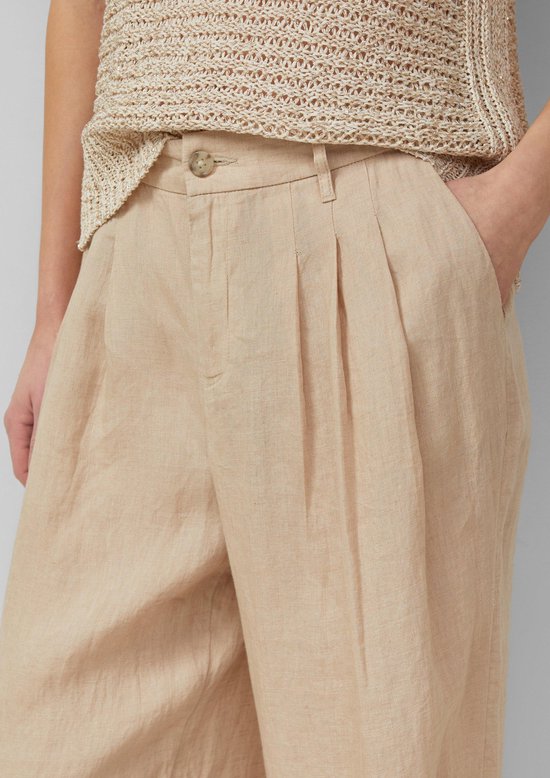 Detailopname van de tailleband van een beige linnen broek met plooien.