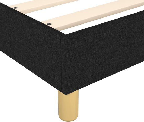Detail van de hoek van een zwart boxspring bedframe met ronde houten poot.