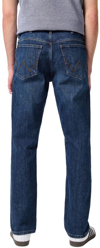 Achterkant van een man in een donkerblauwe jeans met W-stiksel op de zakken, witte sneakers.