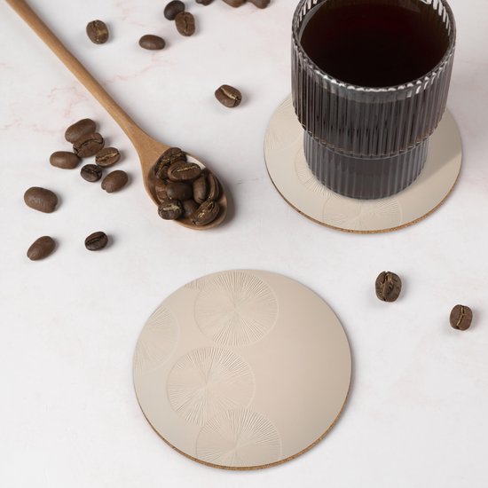 Un sous-verre rond beige à motif de cercles sous un verre de café, avec des grains de café.