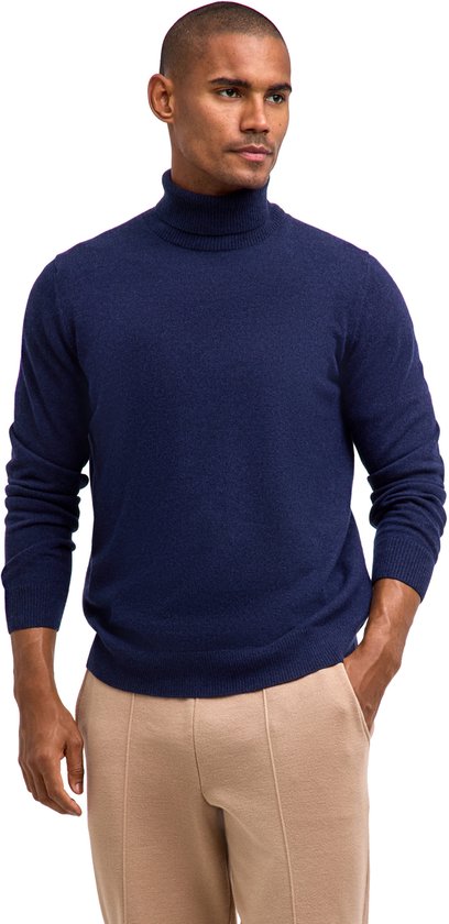 Close-up van man in donkerblauwe wollen coltrui, hand in broekzak, beige pantalon zichtbaar.