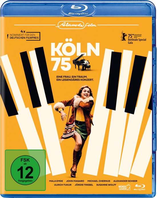 Blu-ray hoes "Köln 75" met vrouw in bruine jas, groene rok en gele top, lopend voor pianotoetsen.