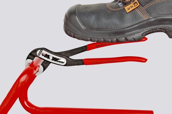 Voet op de rode handvatten van een Knipex Alligator tang die een rode buis klemt.