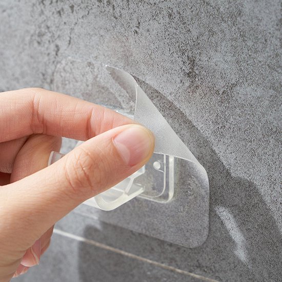 Transparante zelfklevende haak met beschermfolie wordt van de muur verwijderd.