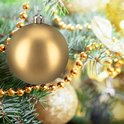 Een grote gouden kerstbal hangt aan een dennentak, versierd met gouden kralen.