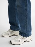 Voeten van een man in een blauwe jeans en witte sneakers.