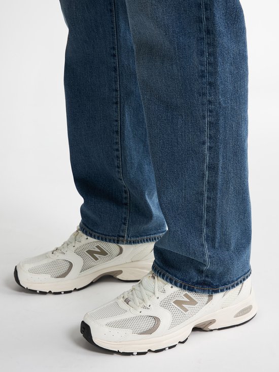 Voeten van een man in een blauwe jeans en witte sneakers.