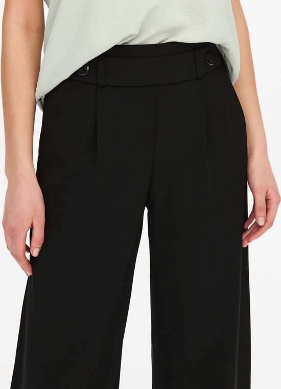 Detail van zwarte wijde broek met hoge taille, knopen en steekzakken.