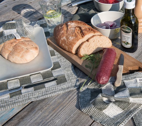 Tafel met eten en gebreide placemats met blokjespatroon in groen en grijs, naast een brood en worst.