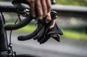 Een persoon houdt een paar zwarte Rogelli fietshandschoenen vast aan het stuur van een racefiets.