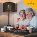 Een ouder echtpaar glimlacht terwijl ze samen aan een legpuzzel werken op een zwarte puzzelmat aan een houten tafel.