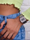 Zilverkleurig Casio horloge op de pols van een vrouw, gedragen met een felgroene top en gebloemde jeans.