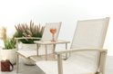 Beige aluminium tuinbank met stoffen zittingen, middenplateau met één roze glas, naast een plant en lantaarn.