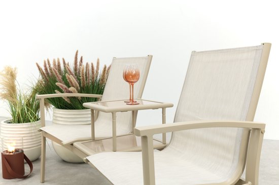 Beige aluminium tuinbank met stoffen zittingen, middenplateau met één roze glas, naast een plant en lantaarn.