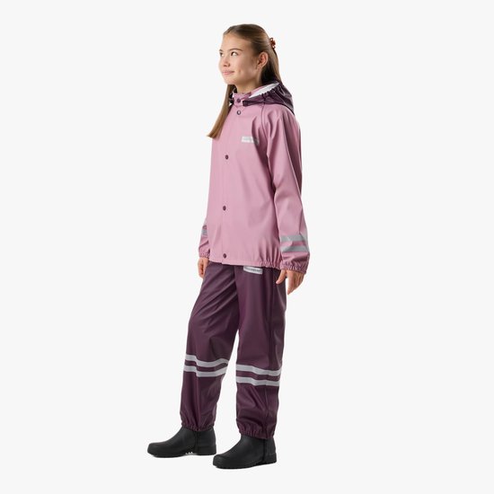 Meisje met lang bruin haar, draagt een roze regenjas met paarse bretelbroek. Reflecterende strepen.