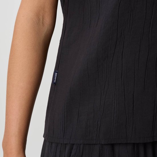 Detail van zwarte Seaside blouse met verticale kreukels en logo label.