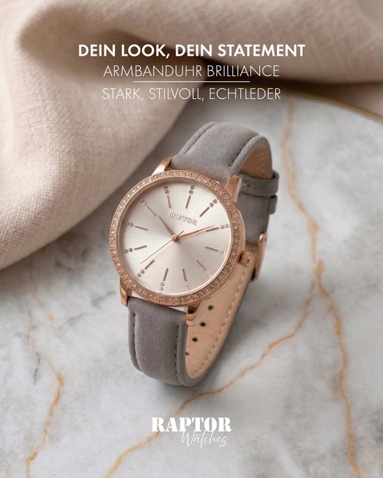 Raptor horloge met grijze leren band en goudkleurige kast bezet met steentjes op een marmeren ondergrond.