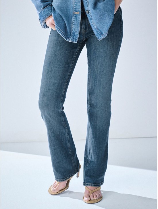 Model draagt een spijkerbroek met bootcut pijpen en hoge hakken.
