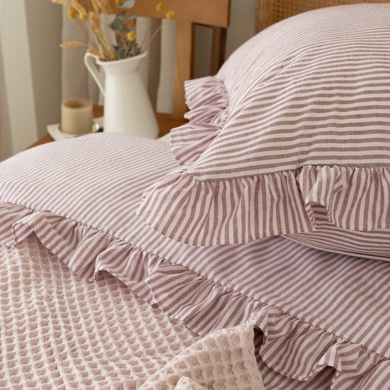 Roze en witte gestreepte kussenslopen met ruches, over een roze wafelsprei.