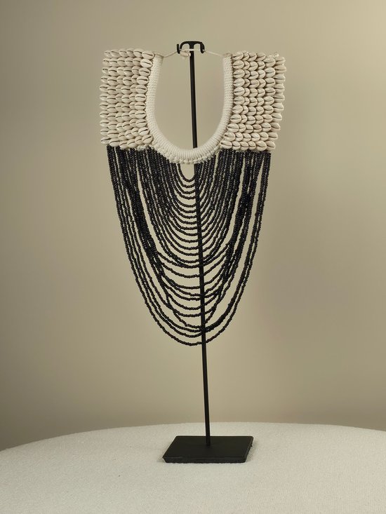 Long collier orné de coquillages blancs en haut, avec des perles noires tombant en cascades multicouches, fixé sur une bande blanche.