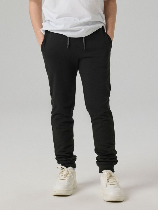Jongen met handen in de zakken van een zwarte joggingbroek.