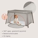 Een baby zit in een grijs reisbedje met 360° gaas voor betere ventilatie en een zij-ingang.