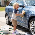Jongen met blonde haren poetst een blauwe auto met een spons, draagt een T-shirt, korte broek en Lilo & Stitch sneakers.
