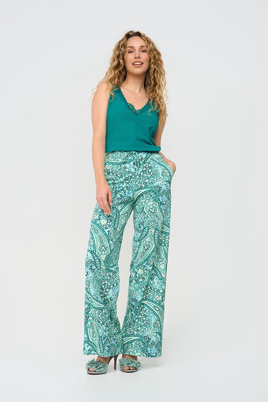 Model in een turkooizen top met kanten randje en wijde palazzo broek met paisley print in groen- en blauwtinten.