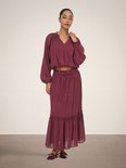 Model draagt een bordeauxrode crop top met pofmouwen en een strikdetail, gecombineerd met een bijpassende lange rok met ruches.